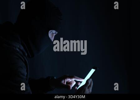 Hacker using mobile phone in dark room, cyber security concept Stock Photo
