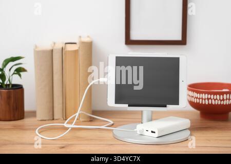 Tablet computer charging from power bank on shelf in room Stock Photo