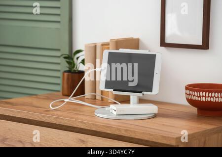 Tablet computer charging from power bank on shelf in room Stock Photo