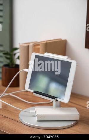 Tablet computer charging from power bank on shelf in room, closeup Stock Photo