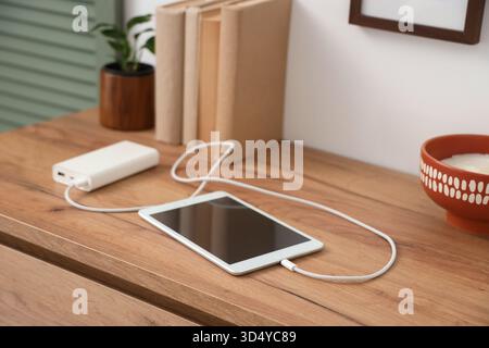 Tablet computer charging from power bank on shelf in room, closeup Stock Photo