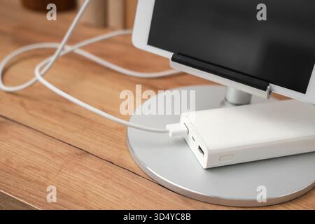 Tablet computer charging from power bank on shelf in room, closeup Stock Photo