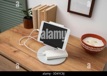 Tablet computer charging from power bank on shelf in room Stock Photo