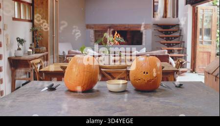 Sitting two carved jack-o'-lanterns glowing on dark island in rustic home, with bowl and knife Stock Photo