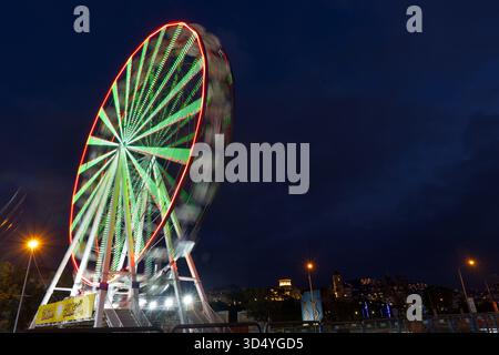 A beautiful 'blue hour' photograph where the soft purple-blue sky meets the bright green and red lights of a rotating Ferris wheel. The motion blur Stock Photo