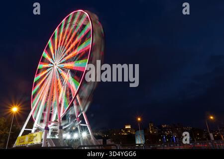 A beautiful 'blue hour' photograph where the soft purple-blue sky meets the bright green and red lights of a rotating Ferris wheel. The motion blur Stock Photo