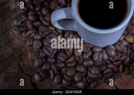 White ceramic cup of dark coffee resting on a bed of aromatic roasted coffee beans and a rustic wooden surface Stock Photo