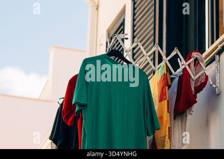 Brightly colored clothing and towels hang from an extended drying rack on a residential balcony. Stock Photo