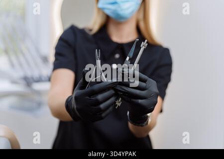 Dentist in mask and black gloves holding sterile dental instruments, clinic closeup Stock Photo