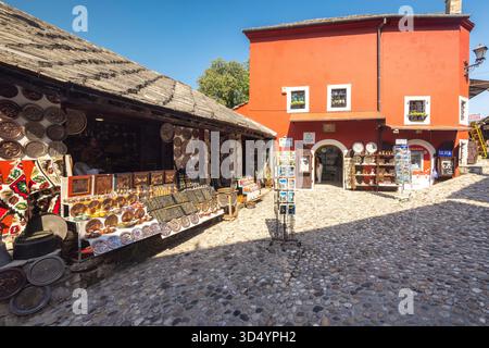 Mostar, Bosnia and Herzegovina - July 9, 2024: Charming shops line a cobblestone street with vibrant red buildings in the background, evoking a sense Stock Photo