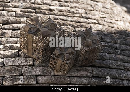 Three decorative gift boxes made of woven material with rustic bows sit on traditional stone Trulli rooftop. Delicate decorations and sturdy stone roo Stock Photo