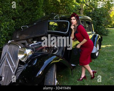 Woman dressed as a 1940s lady in vintage red dress posing with an antique black car Stock Photo