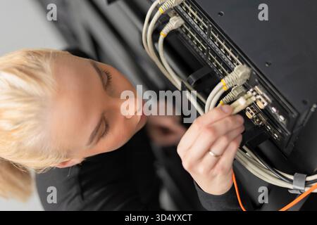 Female IT technician in her 20s working on network equipment in a data center Stock Photo