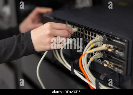 Female IT technician in a datacenter connecting and configuring network switches with cables Stock Photo