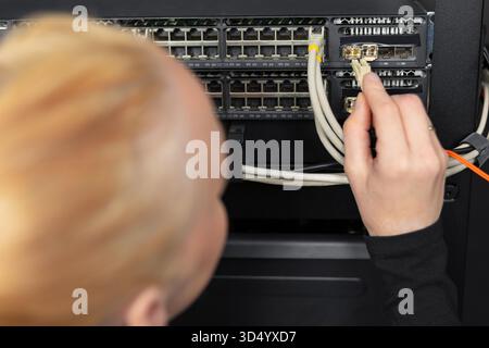 Male IT technician in a data center connecting ethernet cables to a network switch today Stock Photo