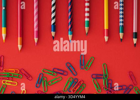 Colorful back to school composition with paper clips and coloured pencils on red background. Learning and creativity concept. Education and time idea. Stock Photo