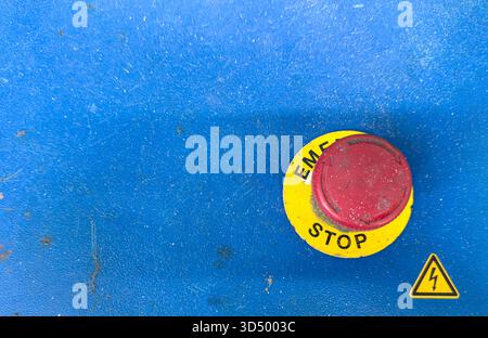 Close-up of a red emergency stop button on a dirty, textured blue industrial control panel. Stock Photo