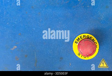 Emergency stop button with yellow "STOP" text and a danger symbol on blue machinery. Stock Photo