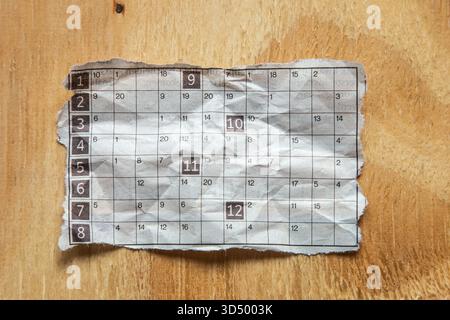 Torn piece of a newspaper puzzle, possibly a number grid or word puzzle, lying on a light brown wooden surface. Stock Photo