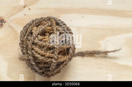 Close-up of a rough, earthy ball of rope or twine on a smooth, light-colored wood surface. Stock Photo