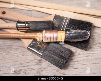 A close-up of several paint brushes with wooden handles and metal ferrules on a light wood surface. Stock Photo