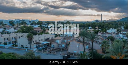 Panoramic shot of a coastal town's rooftops with sun rays breaking through dramatic clouds at sunset. Stock Photo