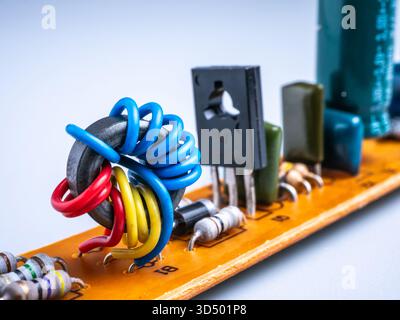 Close-up of an electronic component: a colorful toroidal inductor on an orange circuit board. Stock Photo