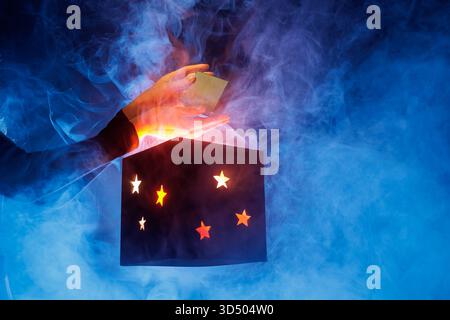 Hands present a small prize above a luminous star box in swirling blue smoke, ideal for surprise promos, unboxing ads, contests, and launch teasers. Stock Photo