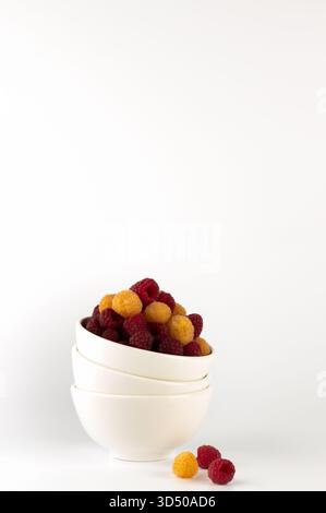 Colorful raspberries and golden berries are neatly arranged in three white bowls stacked together on a plain surface, creating an inviting healthy sna Stock Photo