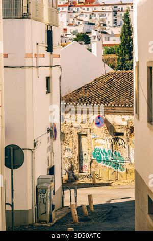 Lagos, Portugal, November 8, 2025. A rundown building with graffiti and a tiled roof stands between whitewashed walls in an alleyway. Stock Photo