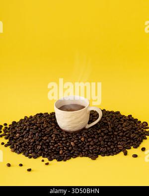 Cup of coffee on roasted coffee beans against yellow background. Minimal coffee concept. Stock Photo