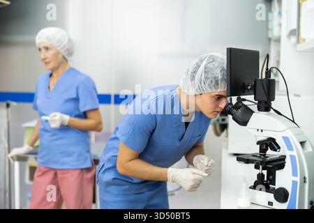 Young veterinarian examining samples under microscope in veterinary office Stock Photo