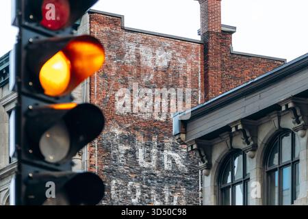 Montreal, Canada - August 11, 2025: Faded vintage sign on old brick wall and yellow traffic light in downtown Montreal, Quebec Stock Photo