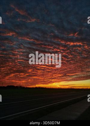 Dramatic sunset with fiery clouds above a rural road and open fields in Belgium. Stock Photo