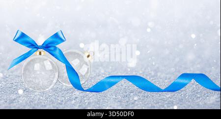 Two transparent Christmas ornaments with blue ribbon and bow on snowy background. Stock Photo