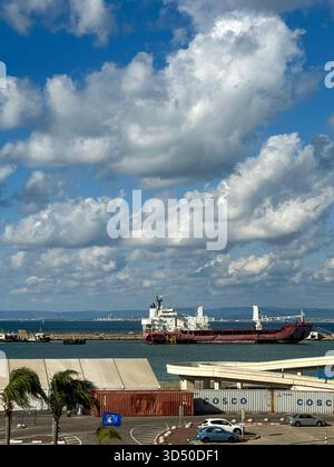 Haifa, Israel, 4 November 2025, A large red and white cargo ship docked in the port, set against the backdrop of a dynamic sky filled with dramatic cu Stock Photo