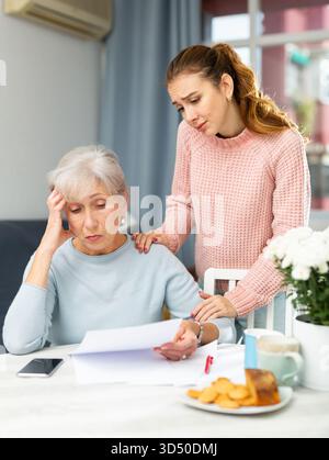 Worried elderly woman with adult daughter checking utility bills Stock Photo