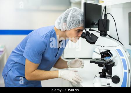 Young veterinarian using microscope to examine blood samples of animal patient Stock Photo
