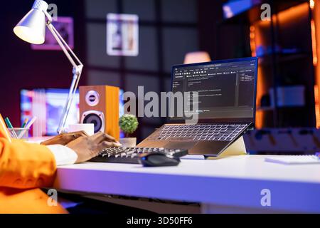 Engineer at desk typing code on notebook device, developing software programs, entering commands. Person at home fixing errors in application, implementing new features, close up Stock Photo
