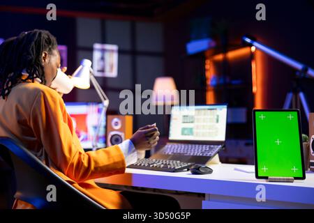 Teleworker in home office completing spreadsheets on laptop next to mockup tablet, entering data, calculating totals. Close up of green screen device next to bookkeeper using spreadsheet software Stock Photo