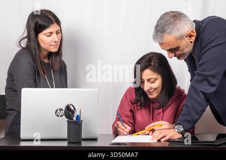 Brainstorming between three colleagues. The two women and the man are about forty years old and are of Italian origin Stock Photo