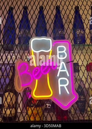 Neon “Bar OPEN” sign glows in pink, blue, and yellow against mesh and bottles—inviting guests into a vibrant nightlife scene Stock Photo