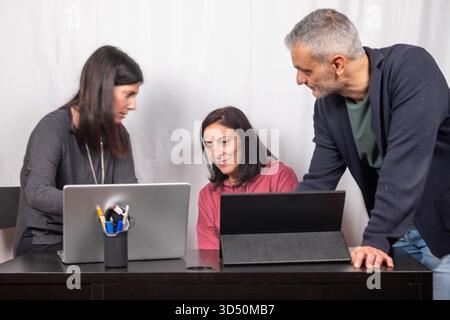 Brainstorming between three colleagues. The two women and the man are about forty years old and are of Italian origin Stock Photo