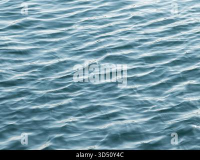 A close-up, high-angle view of the calm ocean surface creating an abstract background texture of small, repeating waves and ripples in a blue-green co Stock Photo
