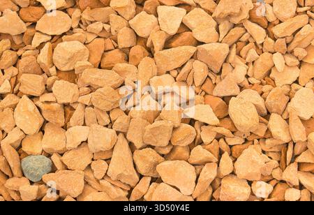 A full-frame background texture of brightly colored orange, peach, and terracotta crushed gravel or small decorative stones Stock Photo