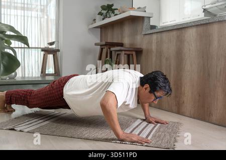 Mature man exercising, holding a plank position on a rug in his living room Stock Photo
