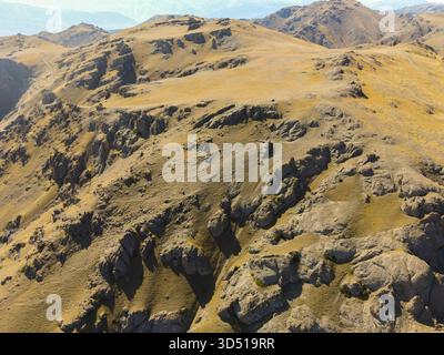 An aerial view focusing on the rough, textured surface of a massive golden-brown arid mountain range with deep gullies and natural rock formations Stock Photo