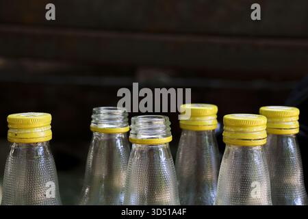 Close up group of empty clear glass beverage bottles with bright yellow caps stand ready for use or recycling, creating sense of order and repetition Stock Photo