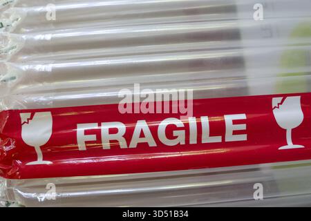 Close up of red fragile warning tape on package with bubble wrap for protection. handling label conveys caution for safe delivery and careful shipping Stock Photo