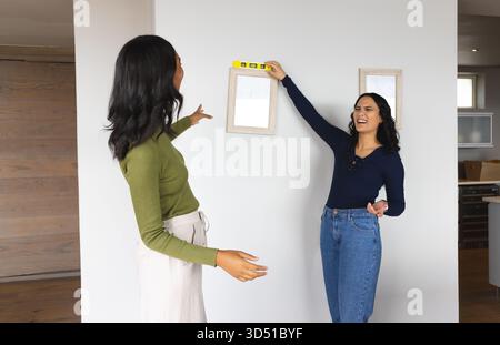 Leveling wood picture frames, Diverse female friends working on home wall, with yellow spirit level Stock Photo